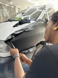 Stagiaire posant un film covering noir sur l'avant d'une voiture – formation covering dans les Yvelines (78)