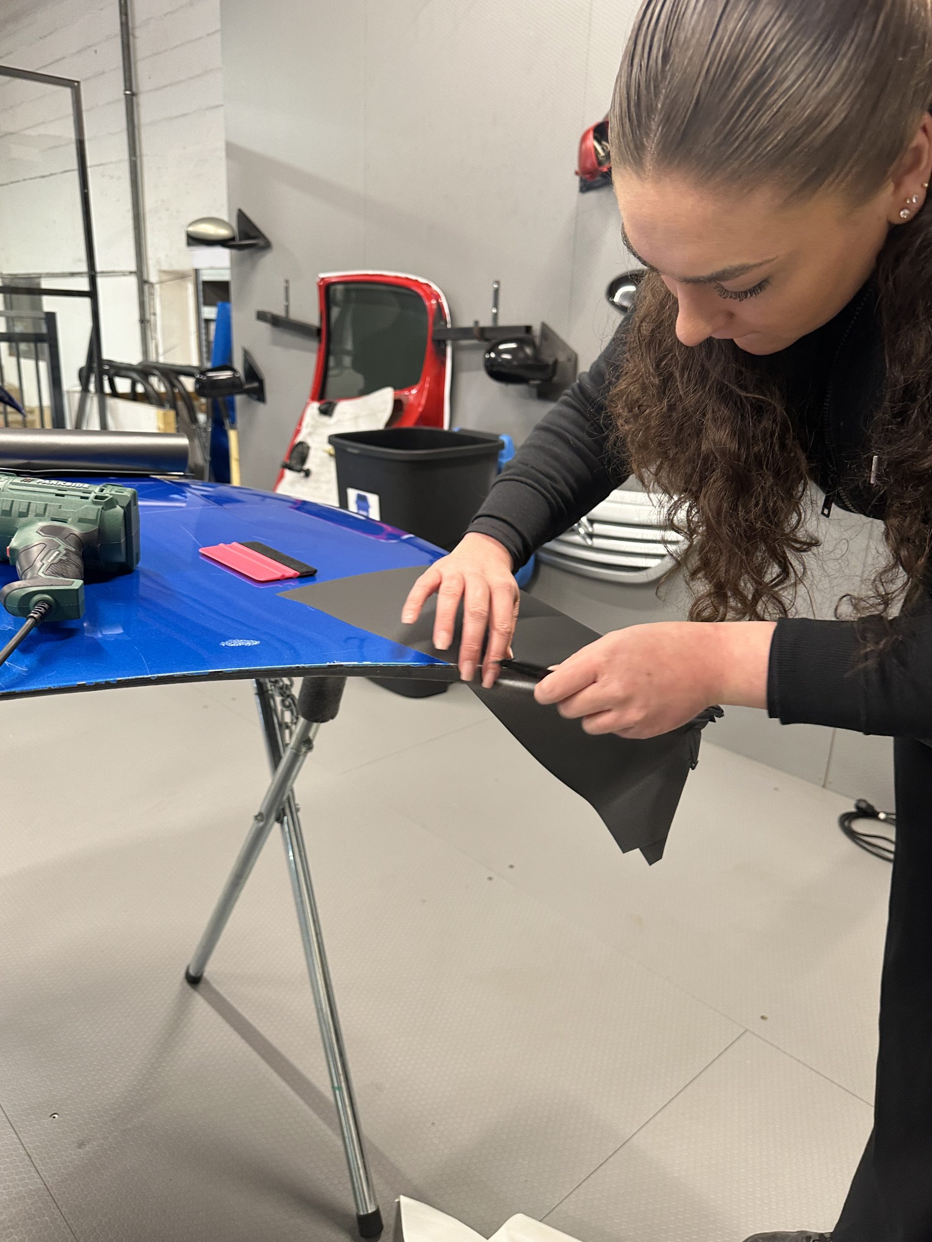 Stagiaire posant un film covering noir sur une pièce de carrosserie – qu'est-ce Que L'enveloppe En Vinyle Pour Les Voitures