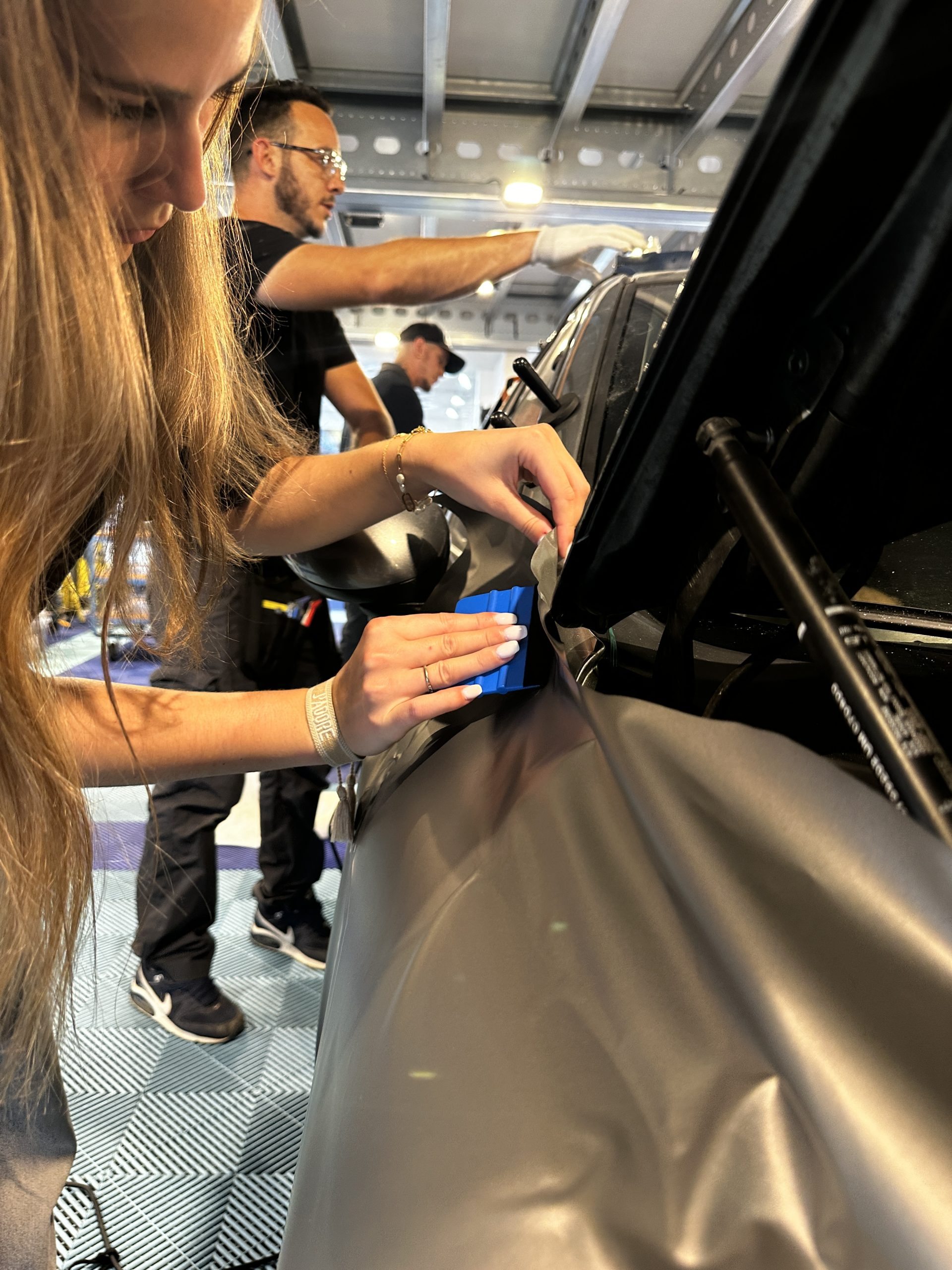 Stagiaires posant un film covering gris sur une voiture – pourquoi une formation complète réduit les abandons en