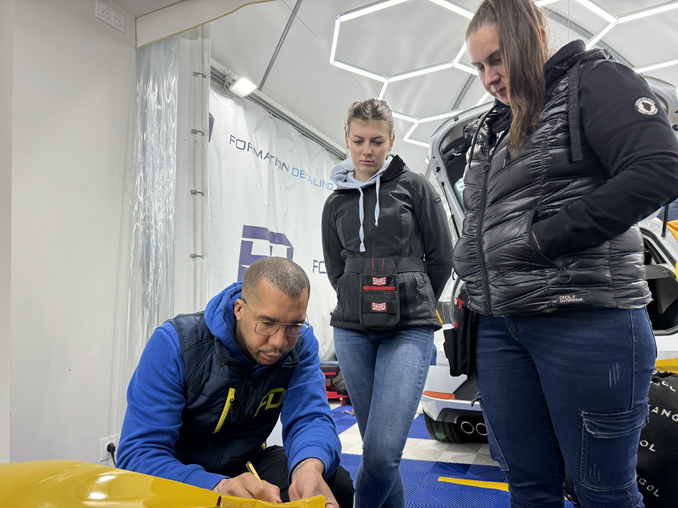 Formateur montrant la pose d'un covering jaune à des stagiaires – décollement des coverings auto en ville en 2025