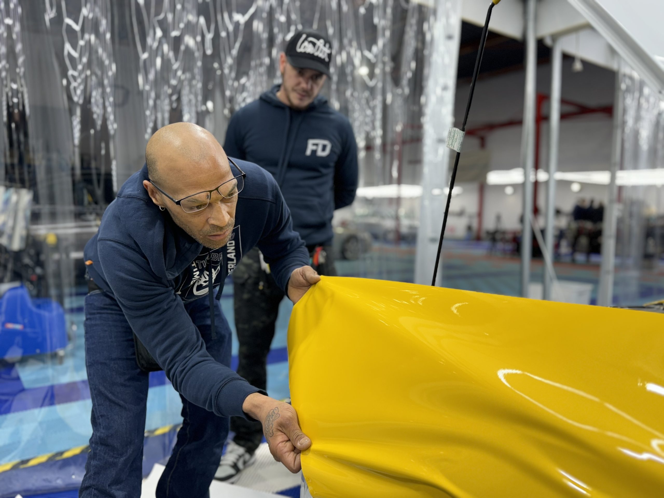 Formateur posant un film covering jaune sur un capot en atelier – prix formation covering