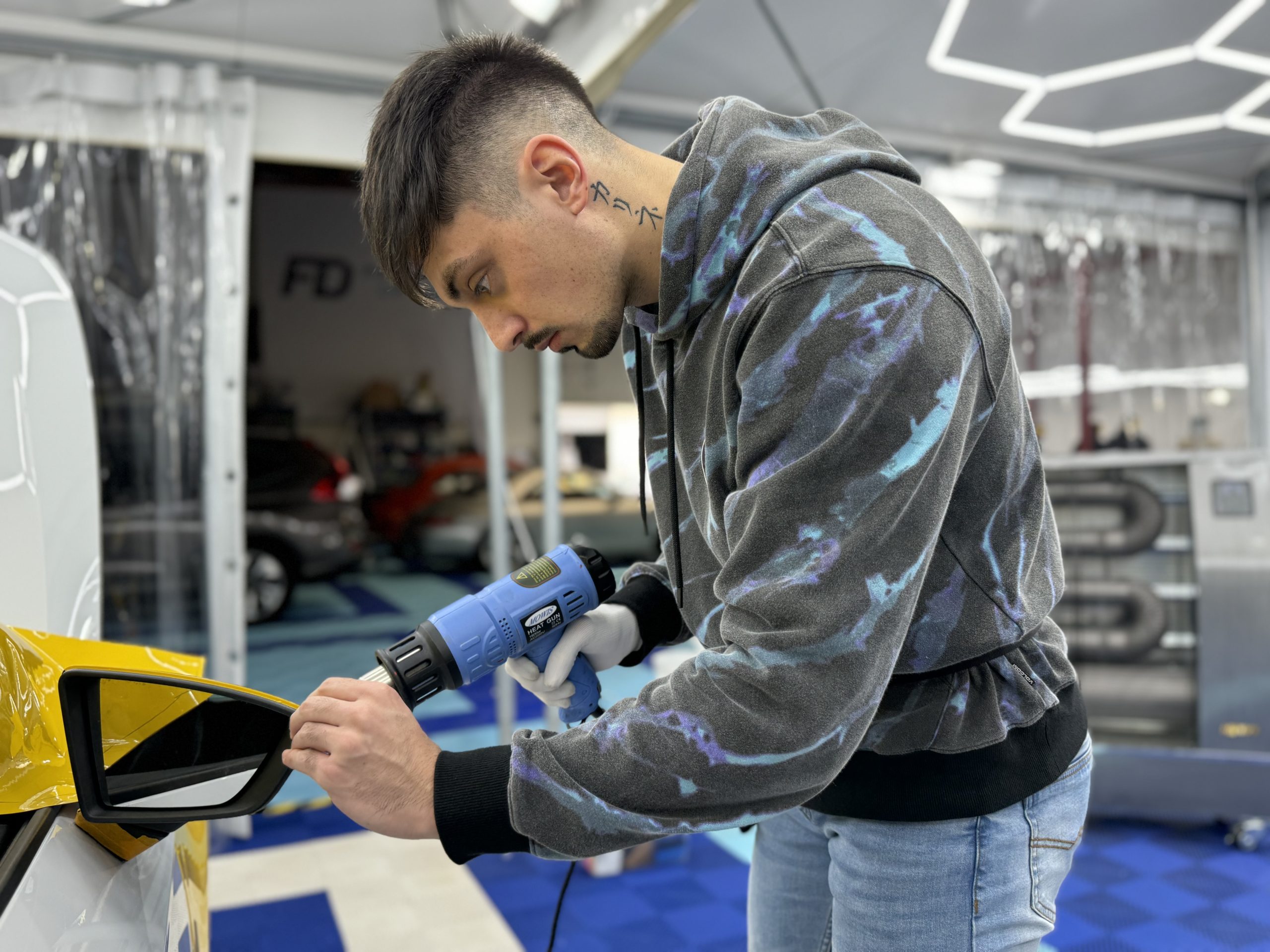 Stagiaire chauffant un film covering jaune sur un rétroviseur – covering ou peinture pour sa voiture