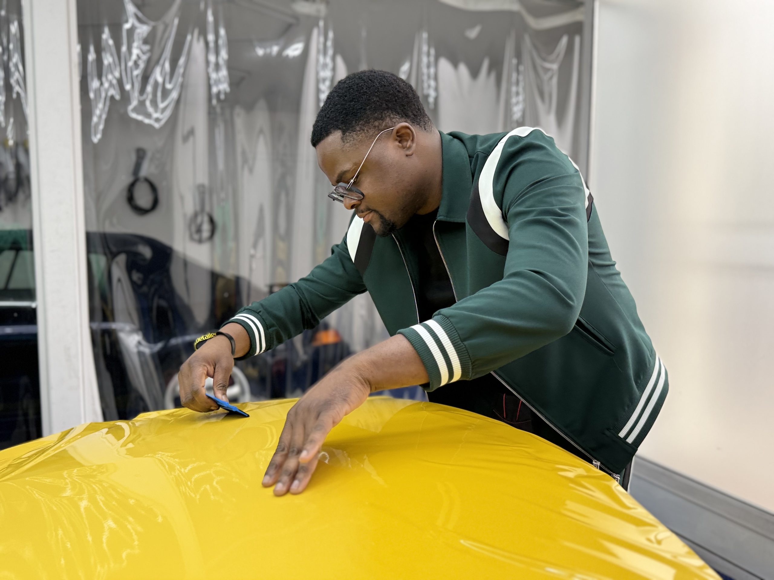 Stagiaire lissant un film covering jaune sur un capot – coût covering auto 2025