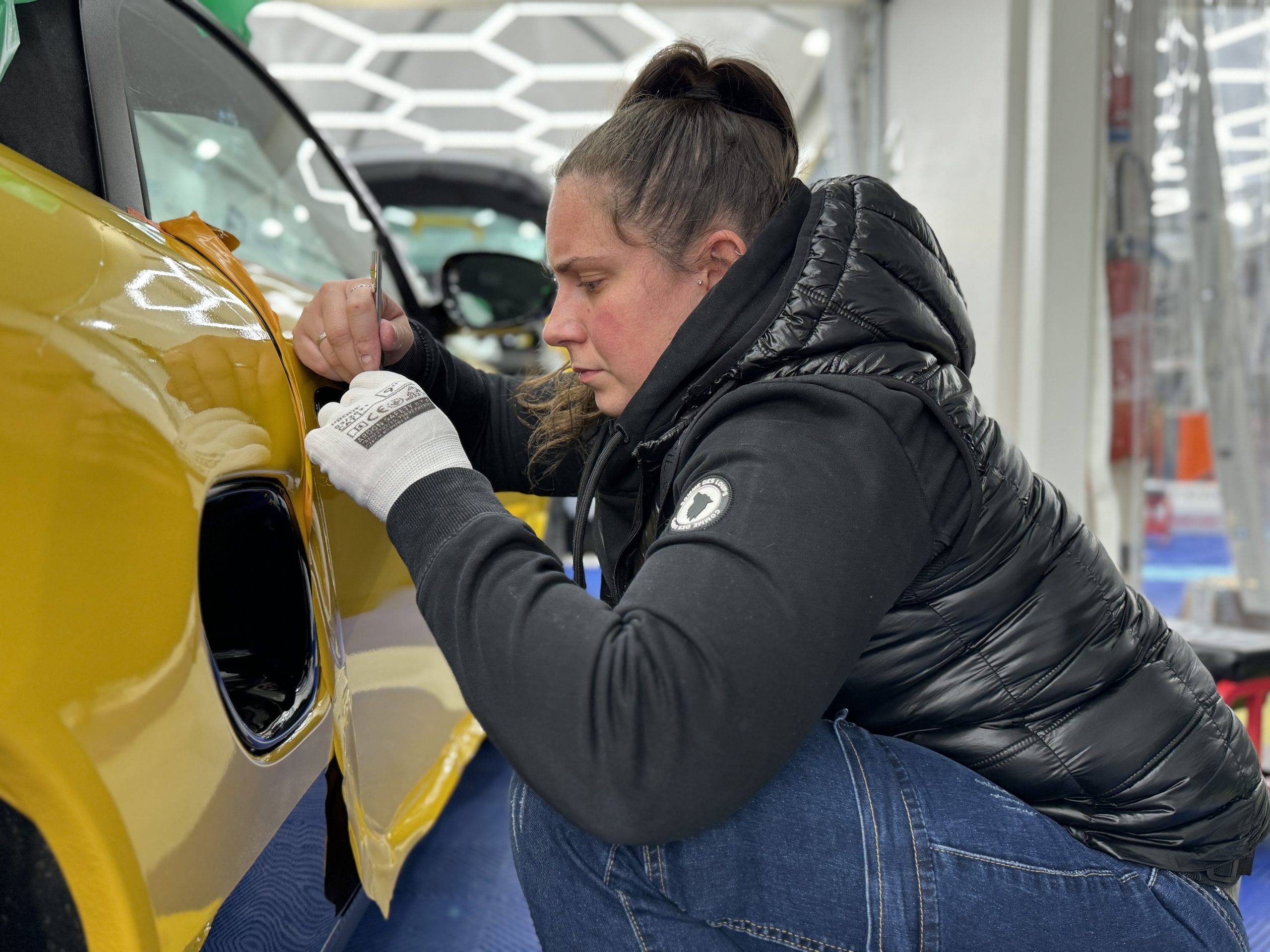 Stagiaire posant un film covering jaune autour d'une trappe à carburant – durée de vie d’un wrapping automobile