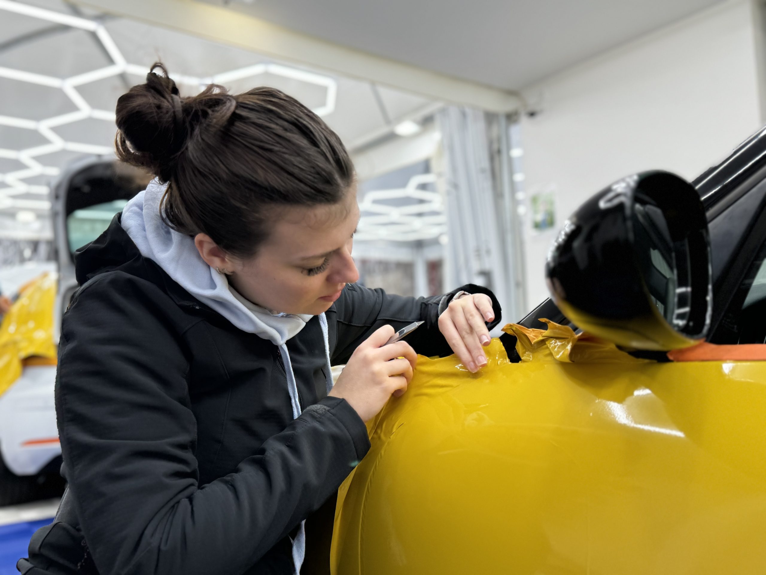 Stagiaire posant un film covering jaune sur une aile – durée de vie d’un wrapping auto