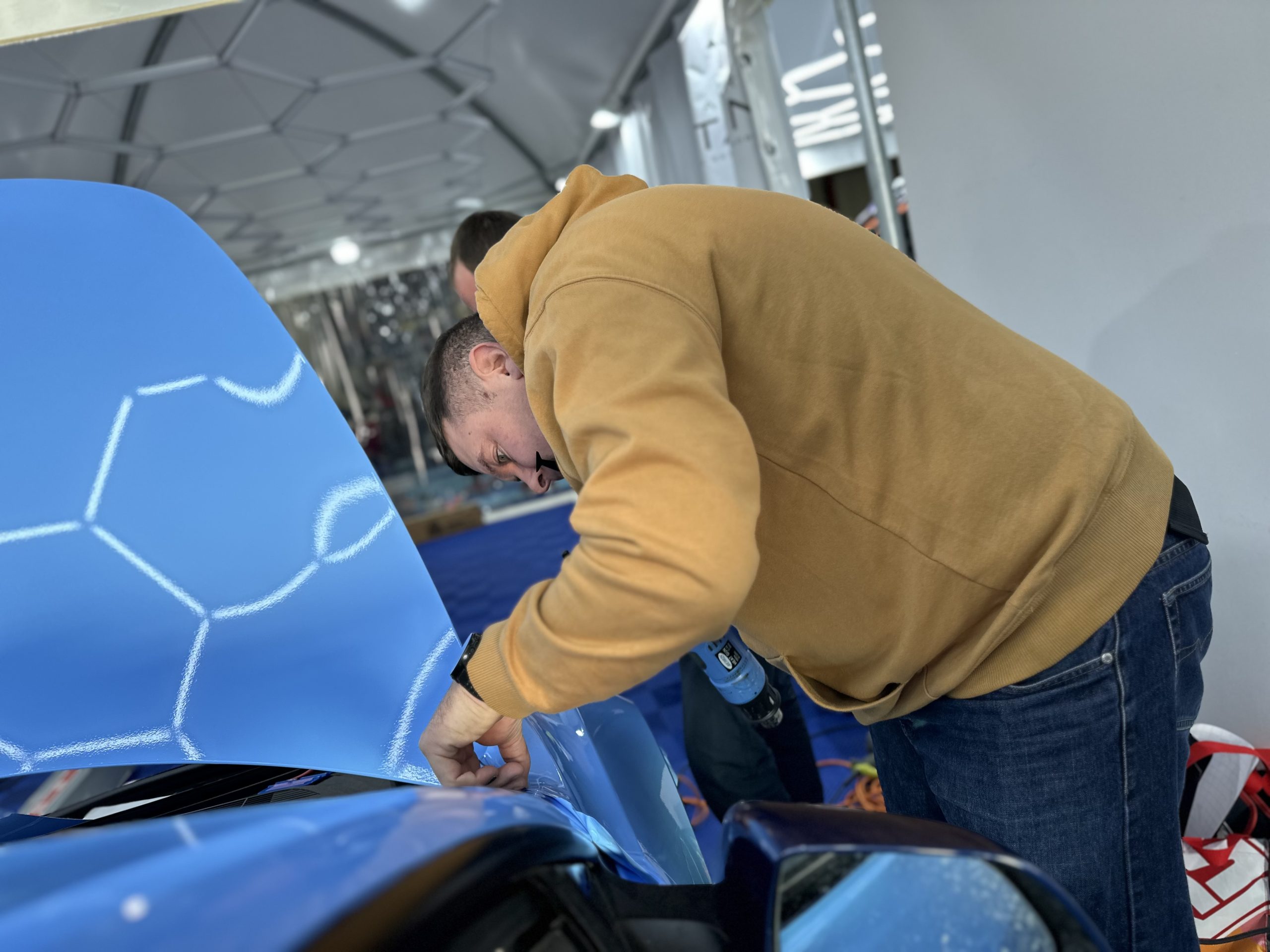 Stagiaire posant un film covering bleu ciel sur un capot – combien coûte un covering de voiture en 2025