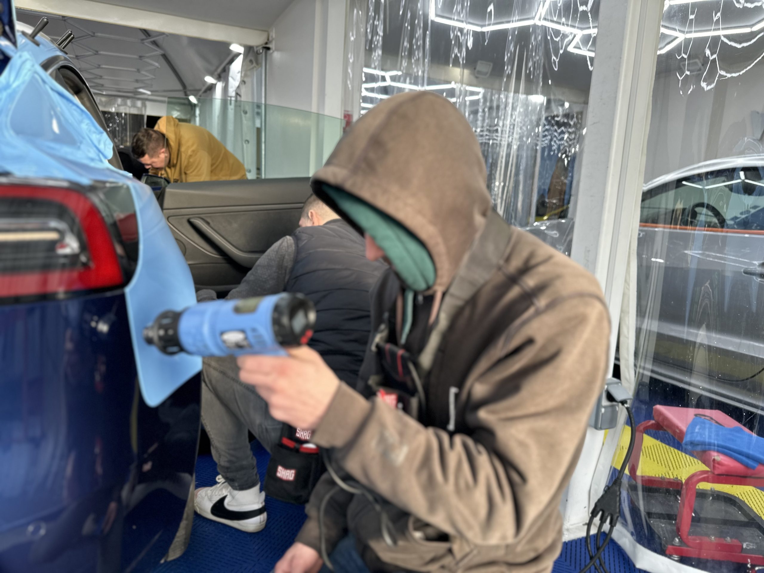Stagiaire chauffant un film covering bleu au décapeur thermique – formation pose covering voiture