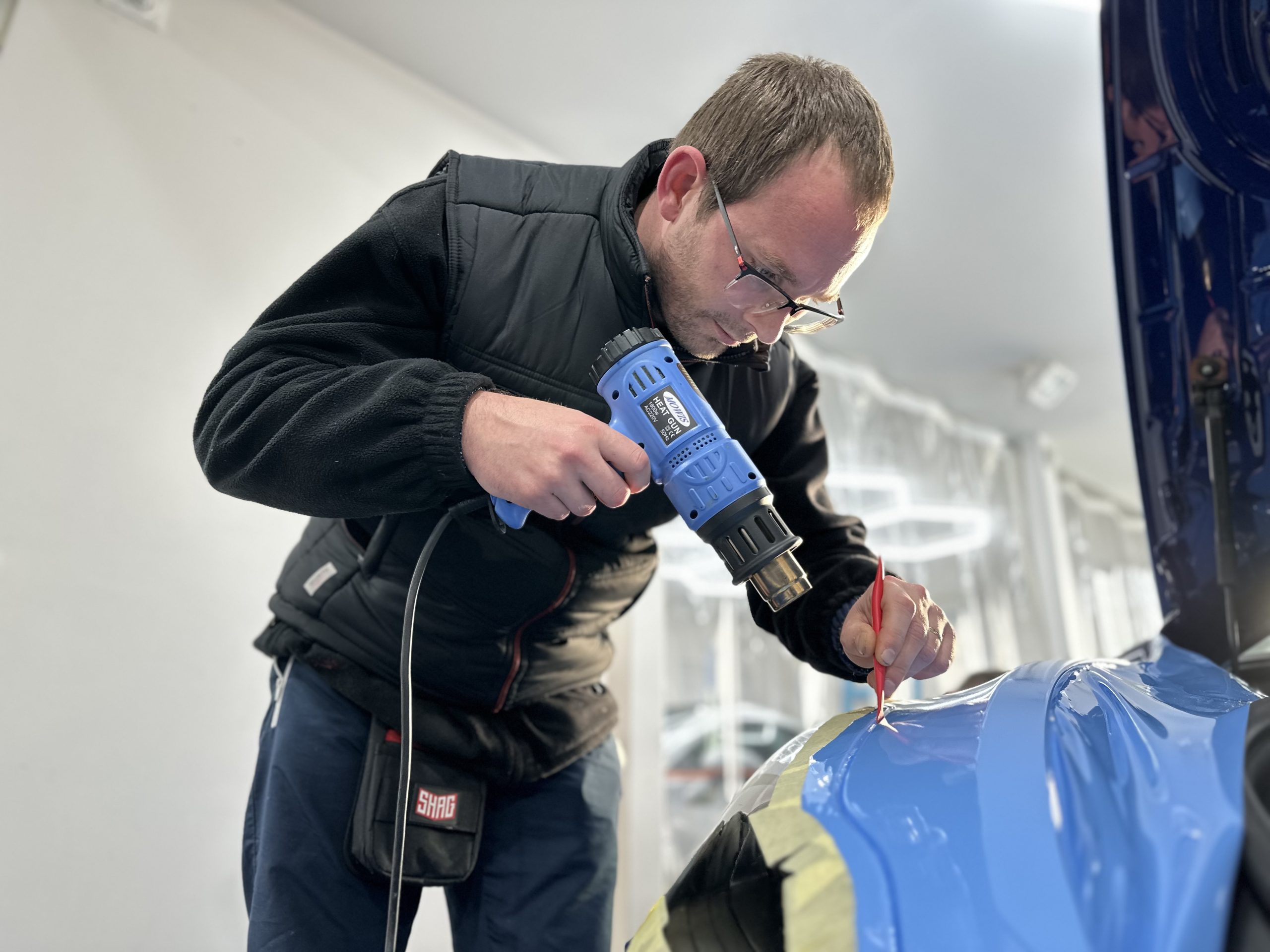 Formateur chauffant un film covering bleu sur une portière – quel budget pour une formation covering automobile