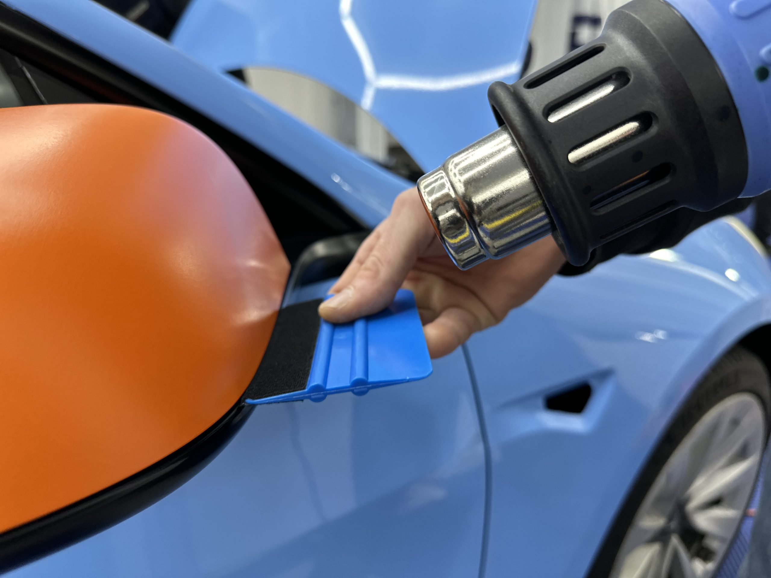 Chauffe d'un film covering orange sur un rétroviseur au décapeur – comment se lancer dans le covering automobile