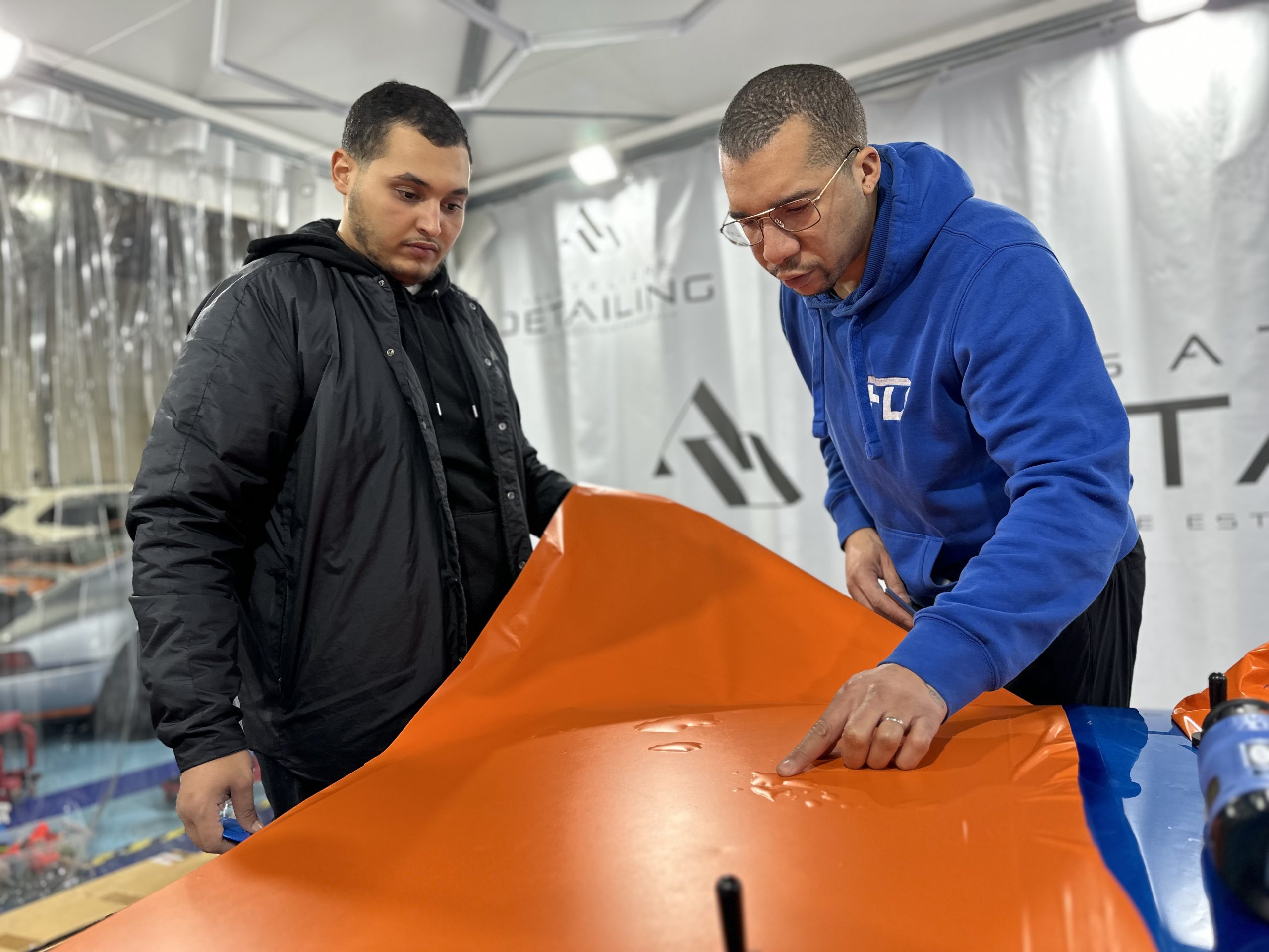 Formateur et stagiaire posant un film covering orange sur un capot – formation pose covering voiture